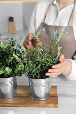 Mutfakta farklı yapay saksı bitkileriyle beyaz mermer masanın yanında bir kadın var.