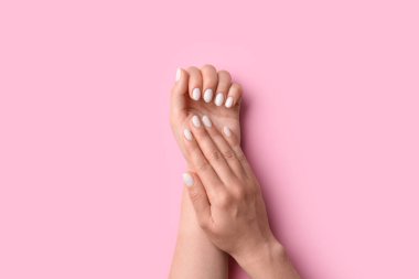Manikürlü ellerini pembe arka planda beyaz tırnak cilası ile gösteren bir kadın.