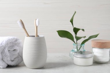 Bambu diş fırçaları tutacakta, havluda, pamukta ve açık gri masadaki yapraklarda.