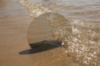 Round mirror reflecting sea on sandy beach clipart