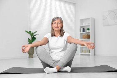 Mutlu son sınıf öğrencisi kadın evde yoga yapıyor.