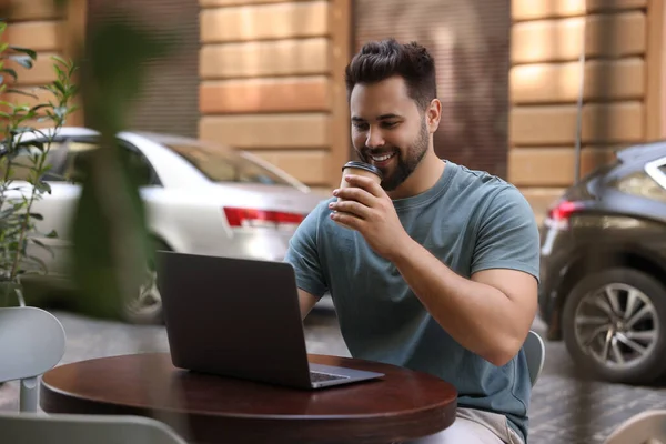 Handsome man with laptop drinking coffee at table in outdoor cafe