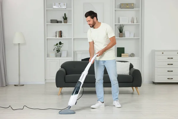 Happy man cleaning floor with steam mop at home
