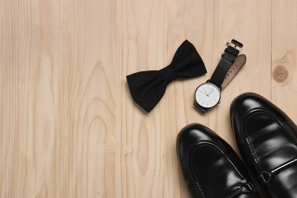 Stylish black bow tie, shoes and wristwatch on wooden background, flat lay. Space for text