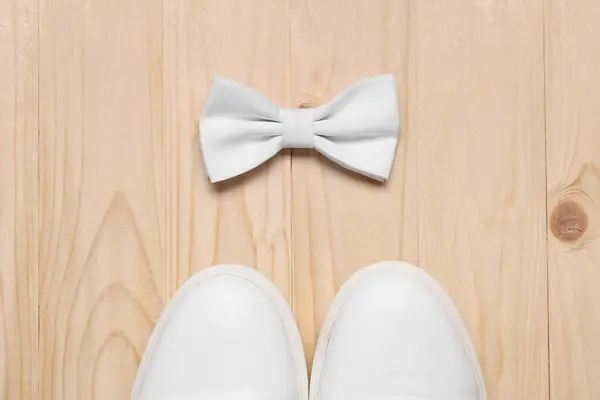 Stylish white bow tie and shoes on wooden background, flat lay