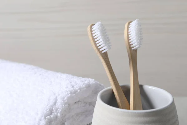 Bamboo toothbrushes in holder and soft towel on light background, closeup