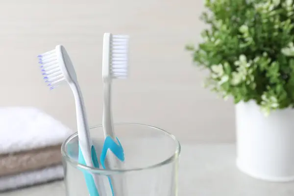 Plastic toothbrushes in glass holder against light background, closeup