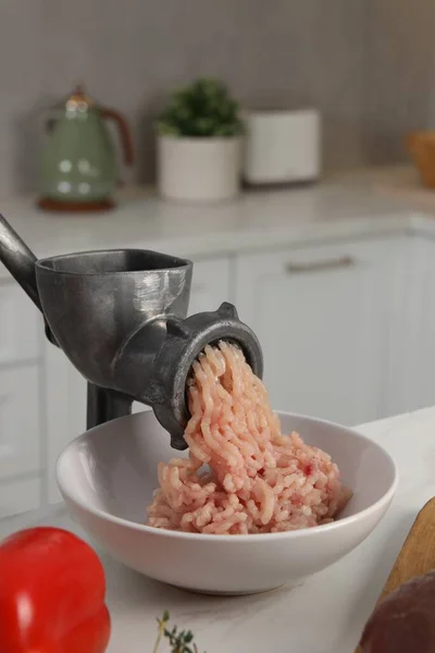 Metal meat grinder with chicken mince and products on white table in kitchen