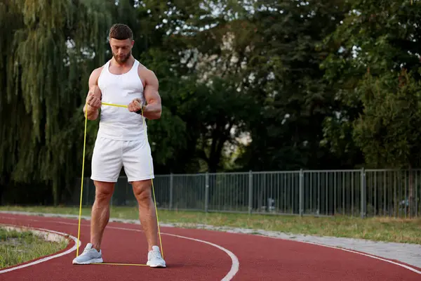 Stadyumda elastik direniş bandıyla egzersiz yapan kaslı adam.