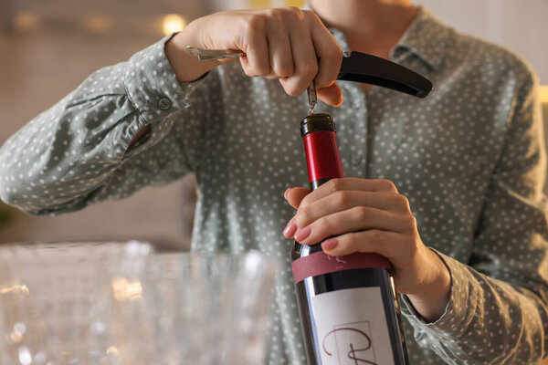 Woman opening wine bottle with corkscrew indoors, closeup