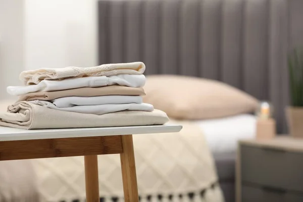 Stack of different folded clothes on bedside bench indoors, closeup. Space for text