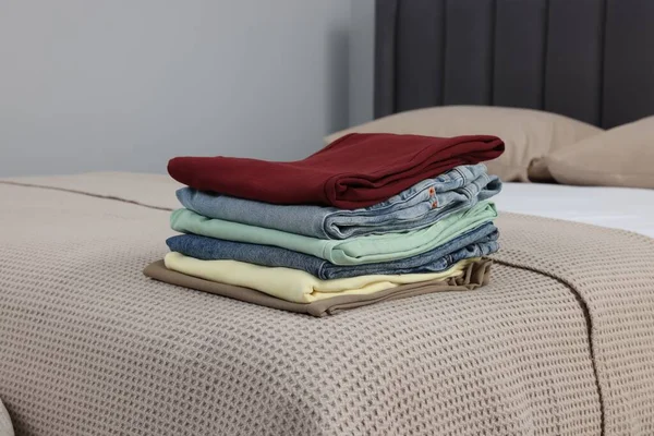Stack of different folded clothes on bed at home