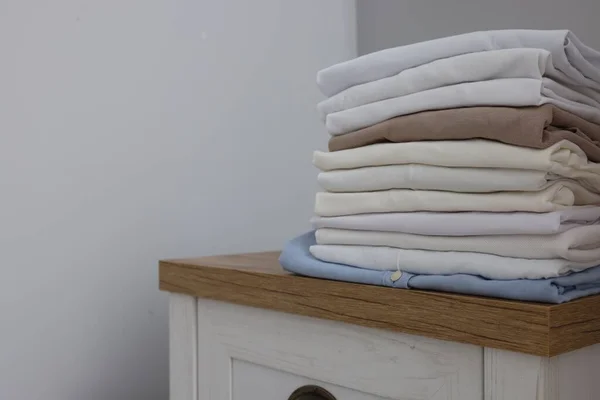 Different folded shirts on chest of drawers near grey wall, space for text. Organizing clothes