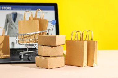 Online store. Purchases, mini shopping cart and laptop on beige table clipart