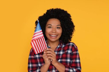 4 Temmuz - ABD 'nin Bağımsızlık Günü. Sarı arka planda Amerikan bayrağı taşıyan mutlu kadın.