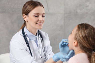 Gülümseyen doktor içeride dil bastırıcı ile kızın ağız boşluğunu inceliyor.