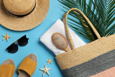 Hasır çanta, palmiye yaprakları ve açık mavi arka planda plaj aksesuarları.