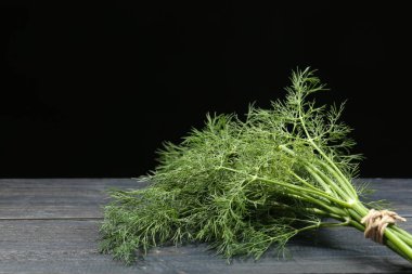 Gri ahşap masada siyah arka planda bir demet taze dereotu. Metin için boşluk