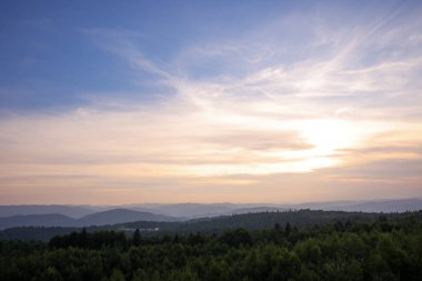 Gökyüzünün altındaki ormanla kaplı dağların resimli görüntüsü.
