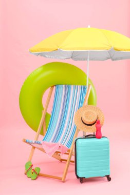Güverte sandalyesi, şemsiye, bavul ve pembe arka plana karşı plaj aksesuarları. Yaz tatili