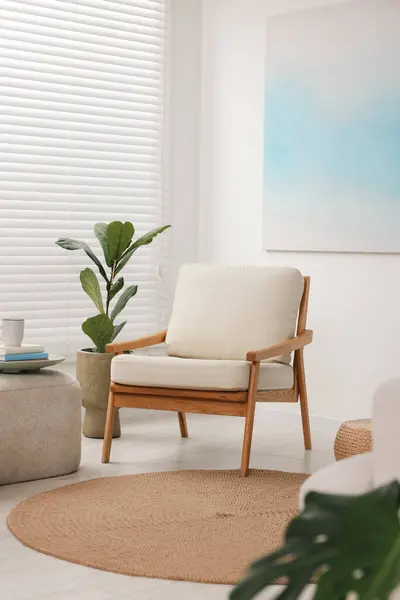 Comfortable beige armchair, ottoman and houseplant in living room. Interior design