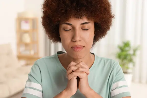 Woman with clasped hands praying to God indoors
