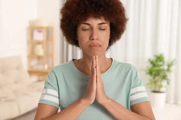 Woman with clasped hands praying to God indoors