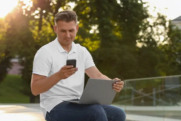 Dışarıdaki bankta akıllı telefon ve laptop kullanan yakışıklı bir adam. Metin için boşluk