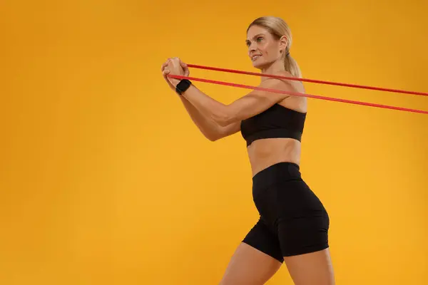 Woman exercising with elastic resistance band on orange background, low angle view. Space for text