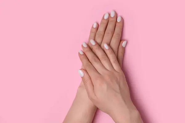 Woman showing her manicured hands with white nail polish on pink background, top view. Space for text