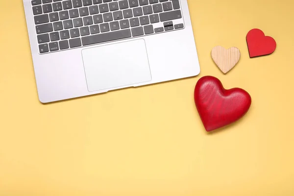 Long-distance relationship concept. Laptop and decorative hearts on pale yellow background, flat lay with space for text