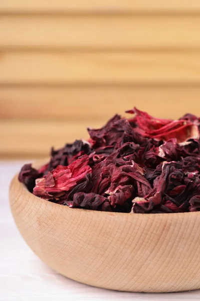 Dry hibiscus tea in bowl on white table, closeup