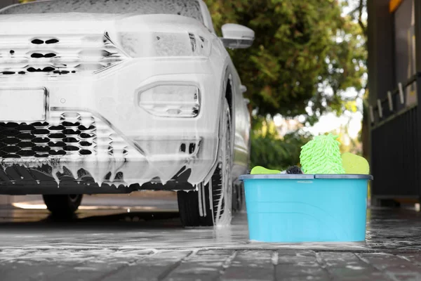 Auto covered with foam and cleaning products in bucket at outdoor car wash