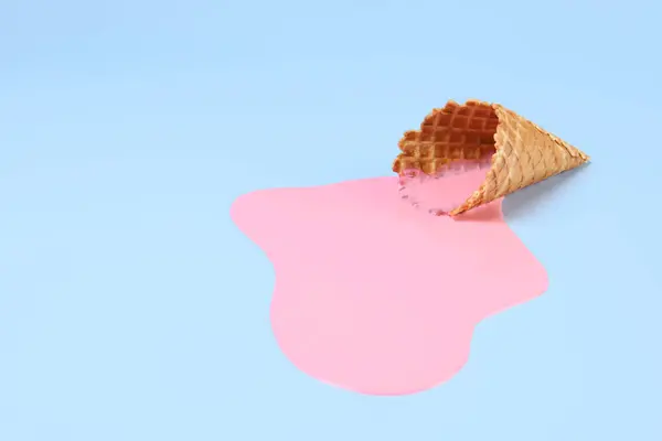Melted ice cream and wafer cone on light blue background, space for text