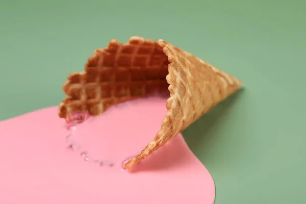 Melted ice cream and wafer cone on green background, closeup