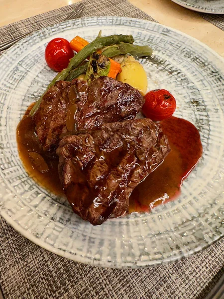 Delicious grilled beef steaks with sauce and vegetables served on table, closeup