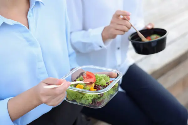 Business people eating from lunch boxes outdoors, closeup