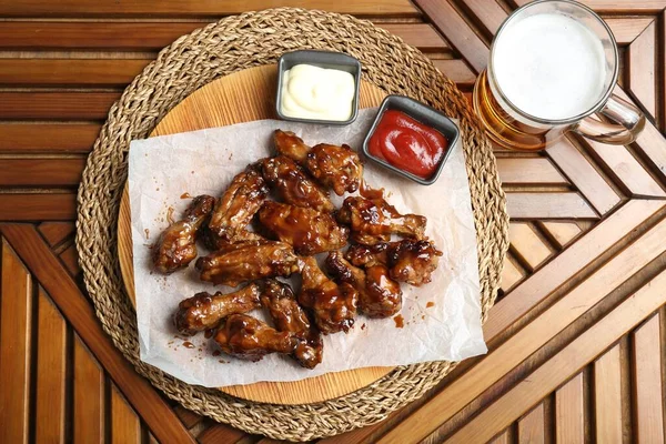 Tasty chicken wings, mug of beer and sauces on wooden table, flat lay. Delicious snack