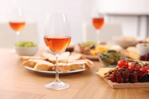 Rose wine and assorted appetizers served on wooden table indoors, selective focus. Space for text