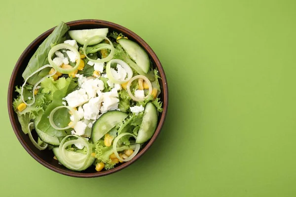 Bowl of tasty salad with leek and cheese on green table, top view. Space for text