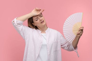 Güzel bir kadın pembe arka planda serinlemek için el sallıyor.