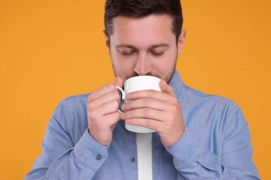 Turuncu arka planda beyaz bardaktan içen adam.