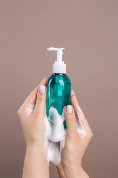 Woman with foam on hands holding bottle of skin cleanser against brown background, closeup. Cosmetic product
