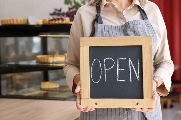 Business owner holding open sign in her cafe, closeup. Space for text
