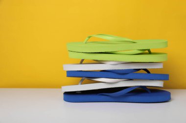 Sarı arkaplana karşı beyaz masada farklı parmak arası terliklerin yığını