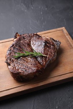 Lezzetli kızarmış biftekli ahşap tahta tahta ve gri desenli masada biberiye.