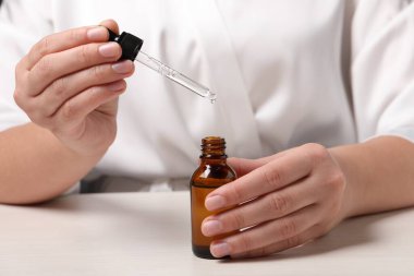 Beyaz masada bir şişe kozmetik serumu ve pipeti olan kadın, yakın plan.