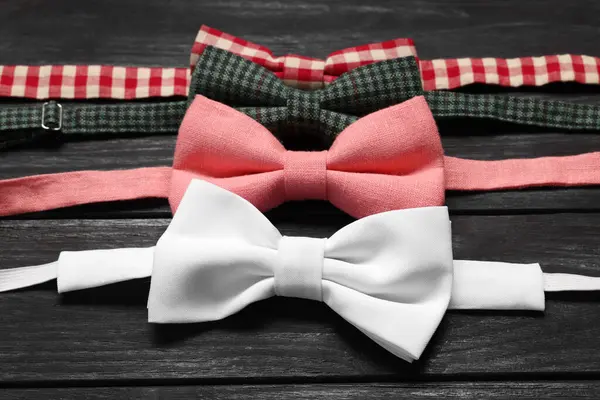 Stylish color bow ties on black wooden table, closeup