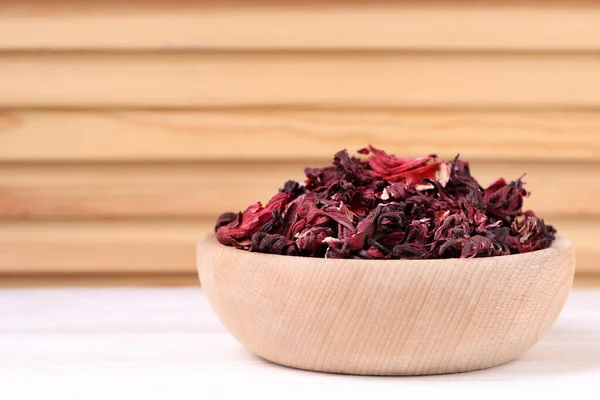 Dry hibiscus tea in bowl on white table, closeup