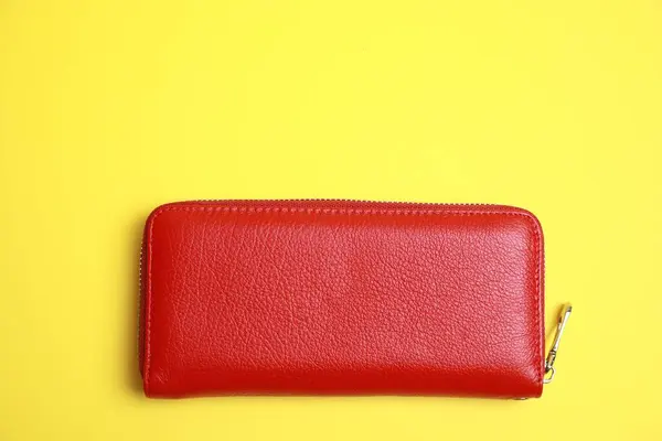 Stylish red leather purse on yellow background, top view